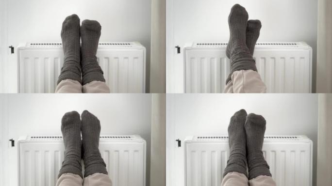 一名妇女在家用取暖器散热器上穿着羊毛保暖袜给冷冻的脚加热