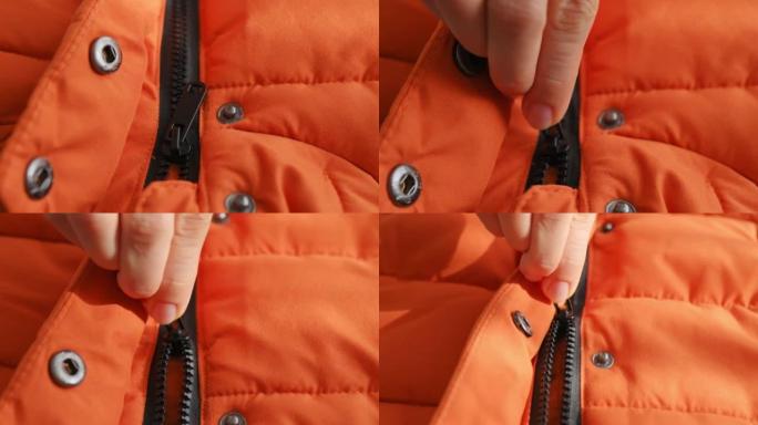冬季橙色夹克、羽绒服上女性双手打开黑色锁的特写。衣服上的开合拉链。秋季防水夹克的细节。纺织品，材料，