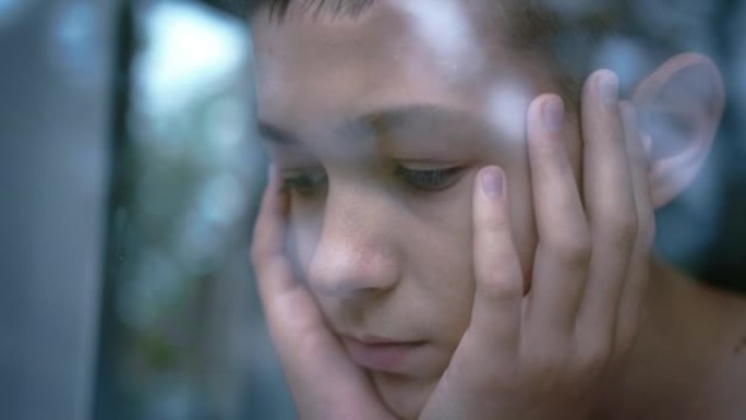 十几岁的悲伤男孩坐着，专心地看着窗外，想着一些事情，移动相机