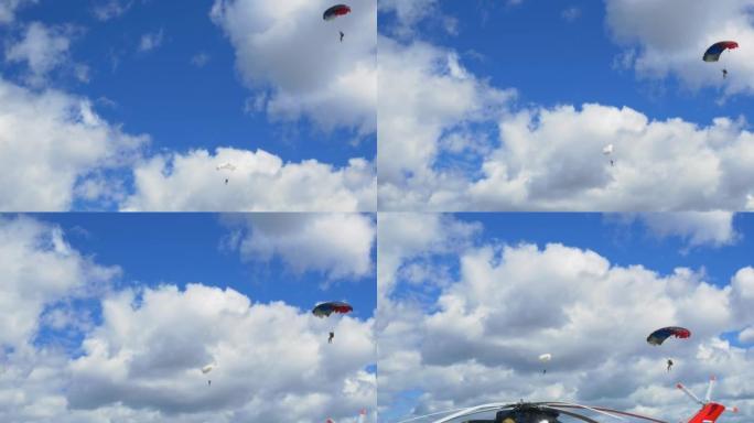 两名跳伞运动员正飞下降落伞，面对美丽的蓝天，白云密布。从两个漂亮的滑翔跳伞运动员的地面上看。极限运动