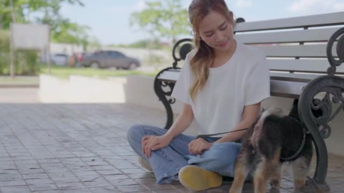 快乐的年轻亚洲女子和她的狗一起玩耍和坐在公园的长凳上。宠物爱好者概念