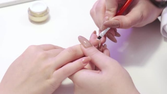 一个女孩在美容院修指甲的特写镜头。指甲护理。美甲师用白色清漆刷指甲的角。美容程序