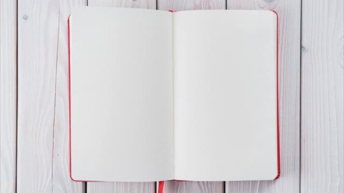红色日记本，白色空纸，在白色木底上从右向左转动无尽。翻页
