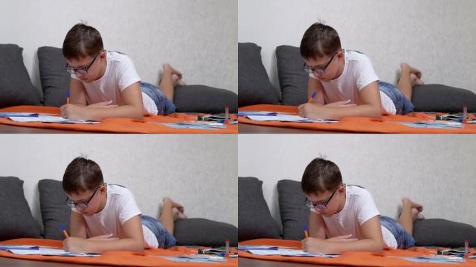 孩子用笔在笔记本上写字，躺在房间的橙色床罩上