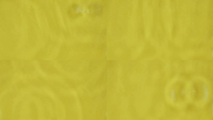 多个水滴落在水面使多个水圈在黄色背景化妆品背景，皮肤水合概念