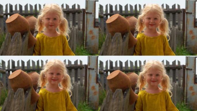 迷人的金发农场女孩在木制村庄围栏附近微笑