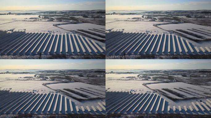 白雪覆盖的可持续发电厂的鸟瞰图，带有许多排的太阳能光伏板，用于产生清洁的电能。冬季可再生电力的低效性