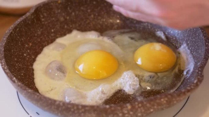 炒鸡蛋煎锅的特写镜头，另一个鸡蛋被打碎以准备煎鸡蛋。炒鸡蛋早餐可以增强一整天的力量。常规准备炒鸡蛋早