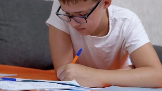 孩子用笔在笔记本上写字，躺在房间的橙色床罩上