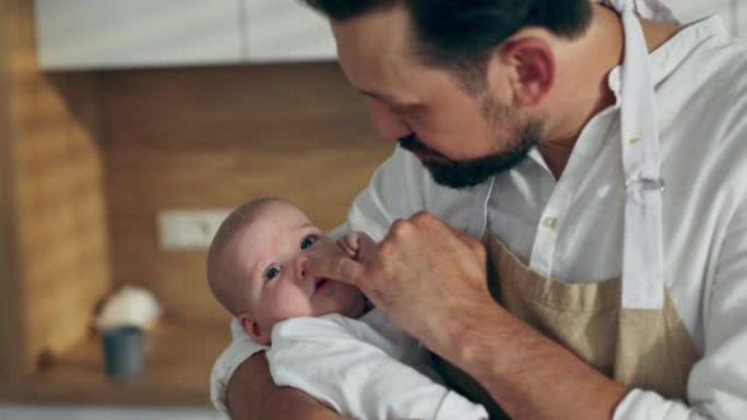 快乐的大胡子父亲手里拿着刚出生的儿子，和站在现代厨房里的婴儿玩耍。父亲婴儿概念。妈妈在家休息时，男人