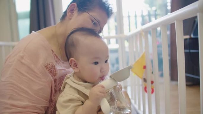 幸福的家庭开朗的亚洲高级妇女祖母抱着照顾可爱的小婴儿蹒跚学步的孙女和拥抱爱，而坐在室内房间在家里，婴