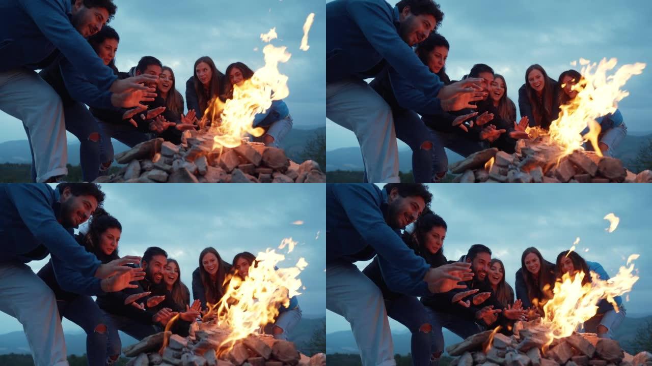 一群朋友在篝火晚会上一起玩乐-友谊生活方式概念与快乐的人旅行者在黄昏夜晚的篝火旁让自己温暖