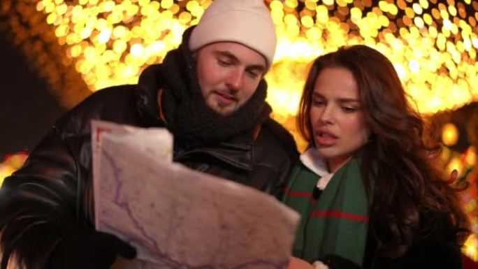 年轻的高加索夫妇在圣诞节之夜在城市中争论方向选择路线。英俊的男人和美丽的女人在户外谈论新年假期计划的