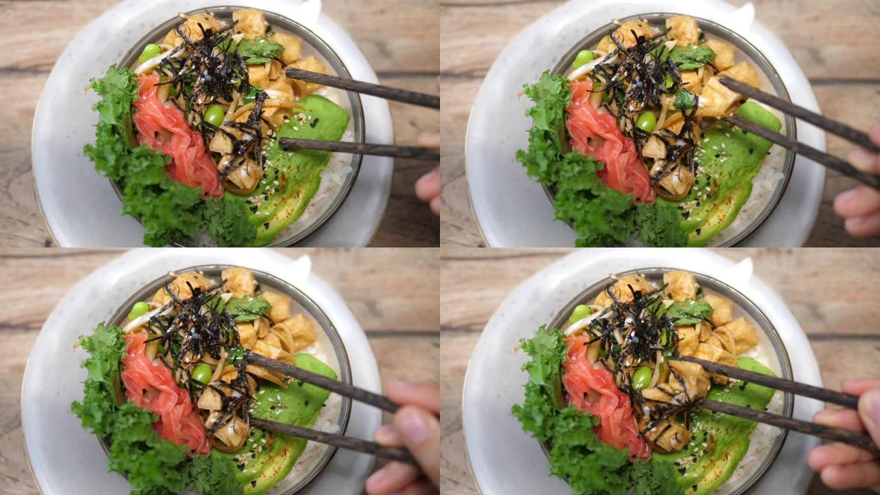 筷子从纯素碗中采摘一块豆腐的俯视图，上面装有海藻，西瓜萝卜，毛豆和鳄梨。健康素食午餐概念。