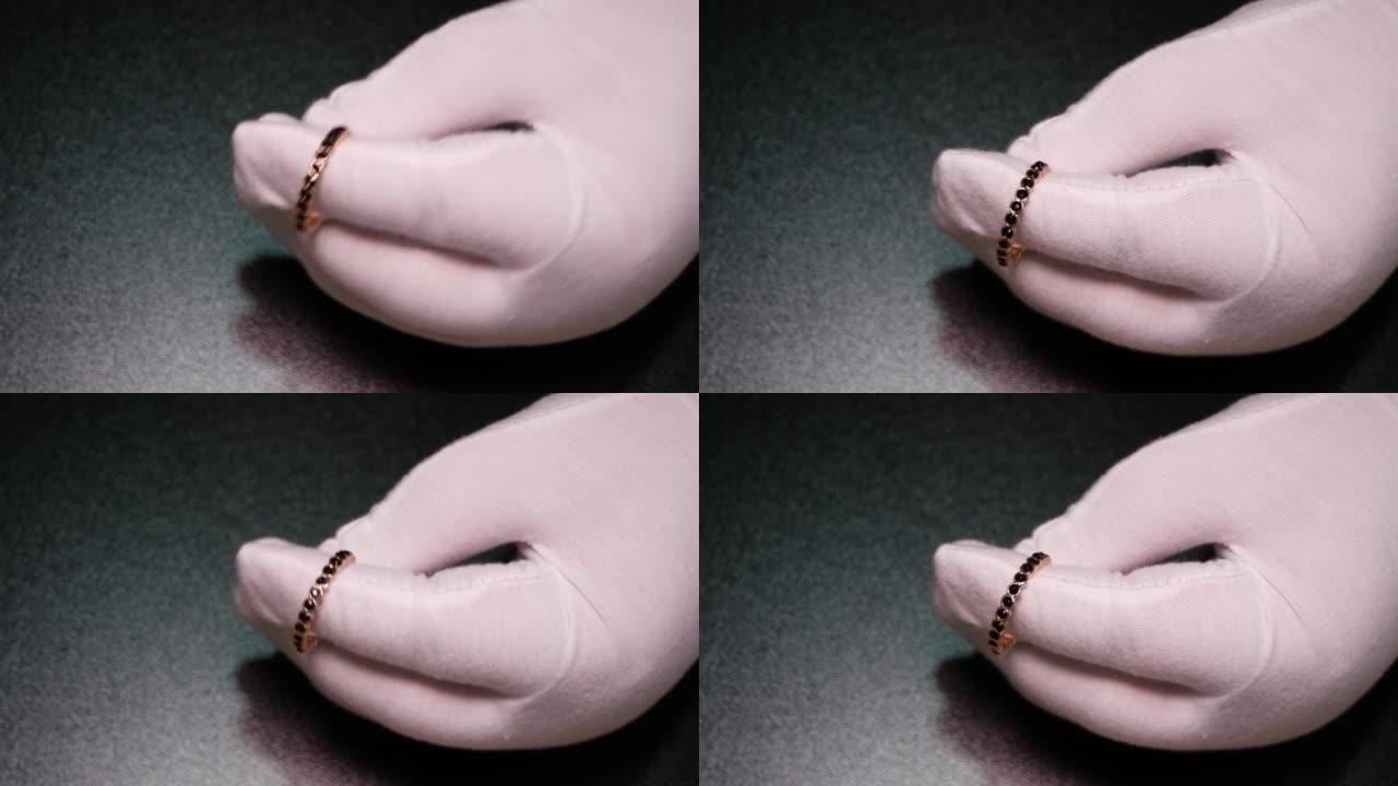 一个戴着白手套的女人的特写镜头，展示了带有黑色立方氧化锆的金戒指