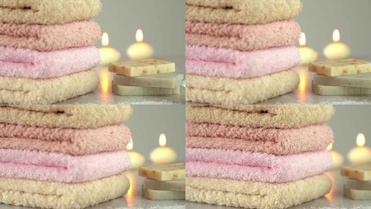 用肥皂和燃烧的蜡烛堆叠的棉质毛圈毛巾。酒店、水疗中心、浴室