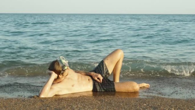 一个戴着潜水面具的人躺在海边，海浪。