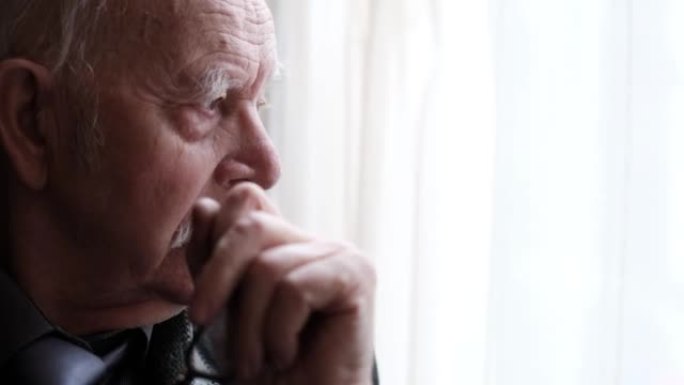 窗户旁沮丧的祖父肖像，特写一位沮丧的老人的肖像