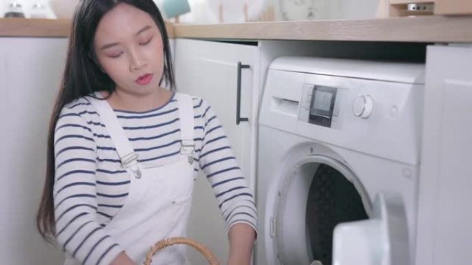 又累又疯的亚洲女人在家洗衣服。沮丧的女孩把衣服放在前面装洗衣机。家务和家务概念