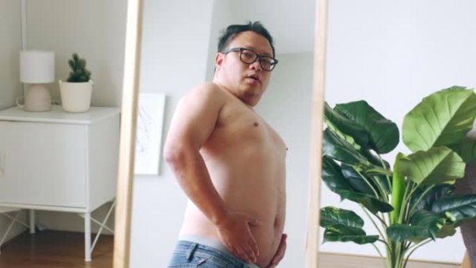 大肚子的亚洲胖子看着镜子里的身体反射，担心肥胖的身体
