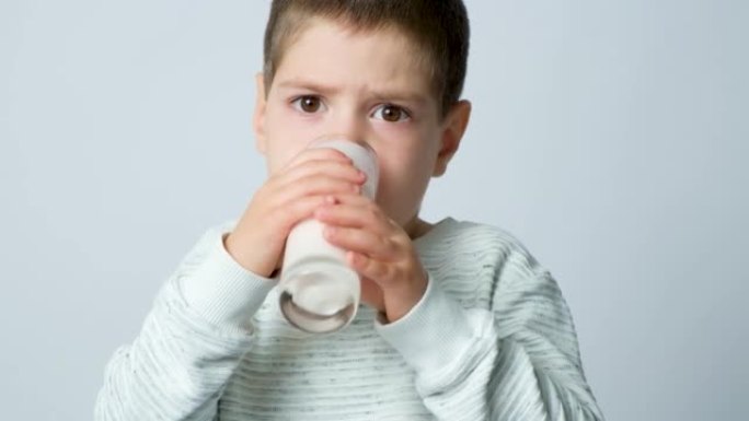 一个可爱的5岁男孩喝开菲尔或牛奶酸奶，并在白色背景下微笑。