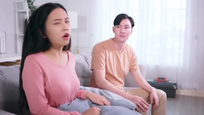 心烦意乱的亚洲男女朋友在家里吵架打架后，一起坐在家里的沙发上。关系问题后，被冒犯的已婚夫妇保持沉默