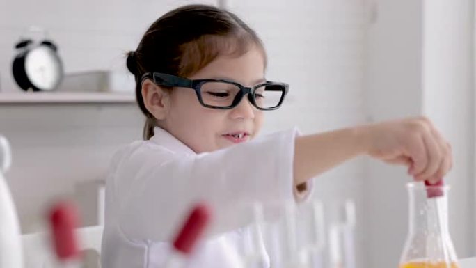 可爱的小女孩穿着实验室外套在学校实验室学习化学，在桌子上的科学课上做分析和混合玻璃中的液体时做化学实