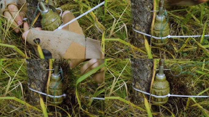 安装一个带绊网的手榴弹。敌人在森林里设下的陷阱。士兵的手和手榴弹的特写。