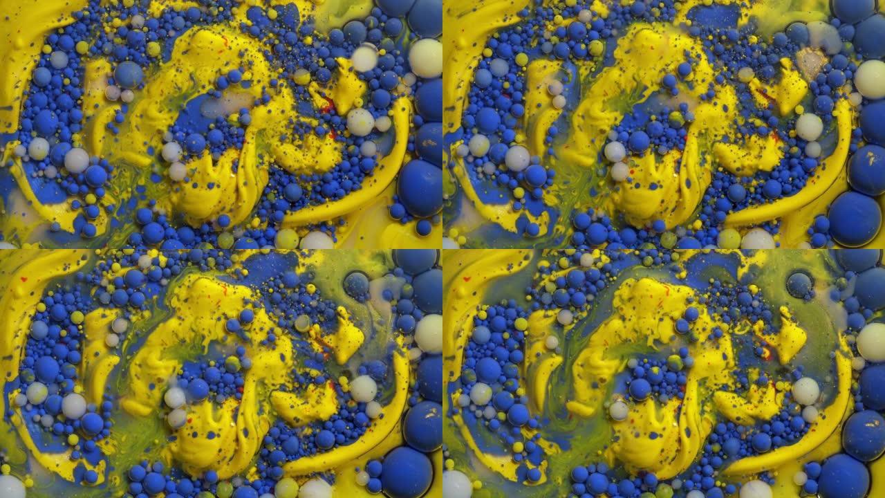 彩色黄色和金色丙烯酸涂料气泡散布在蓝色表面混合在抽象设计中。闪闪发光的颗粒，墨球滴和混合。运动中的多