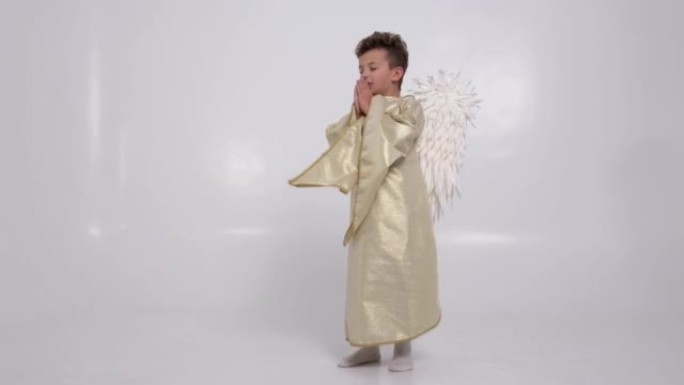 小男孩在白色的工作室中以白色翅膀的天使的形式祈祷他