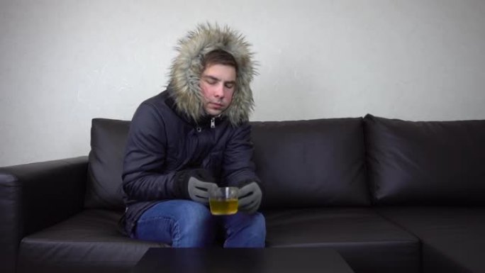一个年轻人穿着冬衣坐在家里，试图保暖。一个人因为逃税而坐在没有暖气的沙发上。4 k