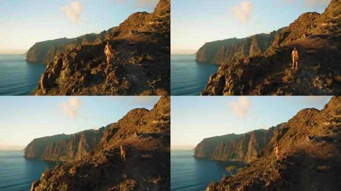 年轻女子走在悬崖顶上，眺望大海。爬山的女孩观察自然之美。美丽的日落天空。