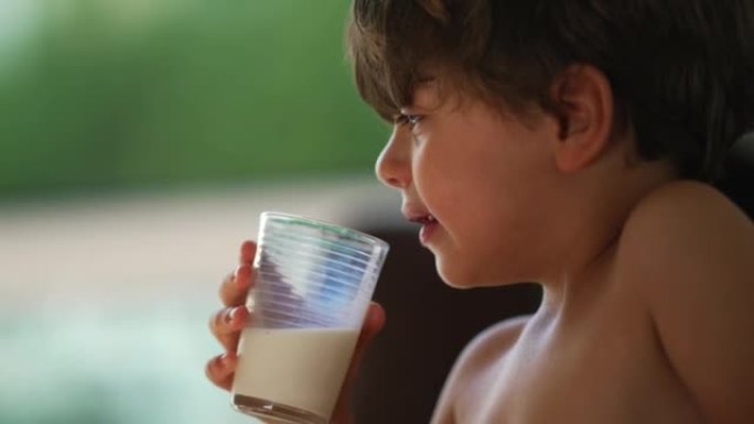 一个沉思的孩子喝牛奶。光着膀子的小男孩在沉思中喝高蛋白饮料