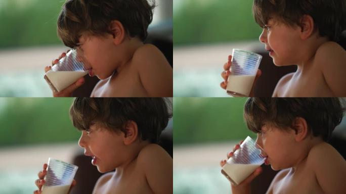 一个沉思的孩子喝牛奶。光着膀子的小男孩在沉思中喝高蛋白饮料
