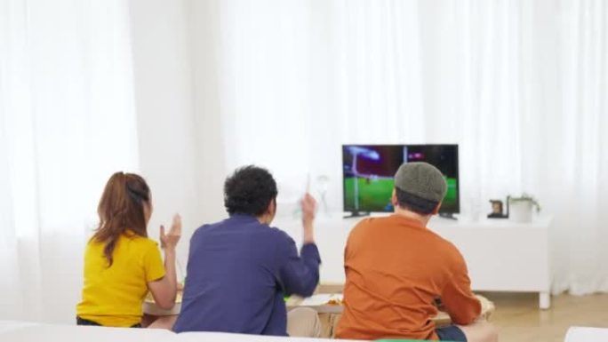 一群亚洲男女朋友一起在家看电视上的体育比赛。