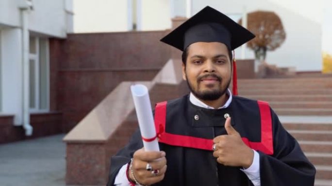 快乐的印度学生毕业生带着文凭站在楼梯上，在大学校园里竖起大拇指