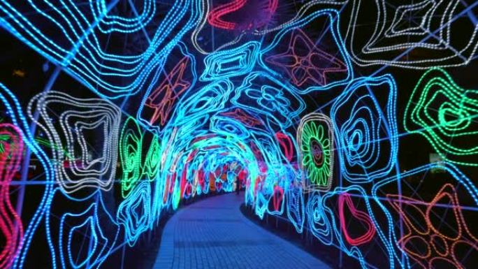 走在迪拜市夜晚辉光公园发光装饰照明的发光隧道中