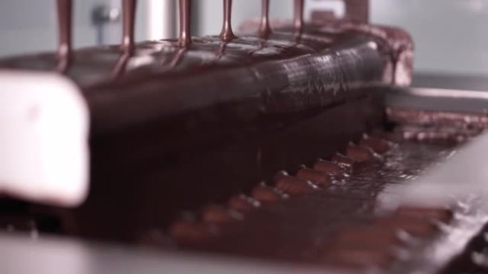 巧克力糖果棒生产-食品工业流程。热液体巧克力射流在传送带上移动的糖果棒上向下流动