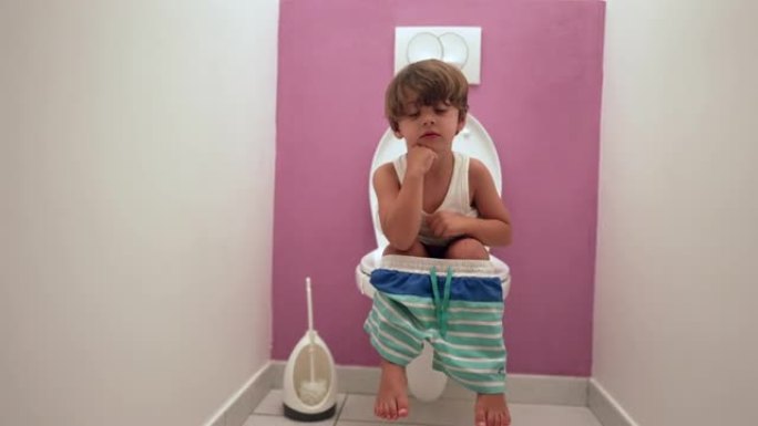 一个可爱的小男孩坐在马桶座圈上，在浴室满足他的需求