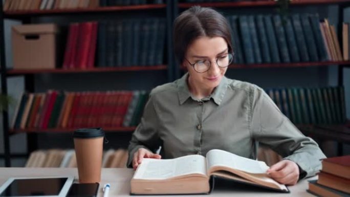 微笑的美女在公共图书馆的桌子上看书翻纸考试大学讲座