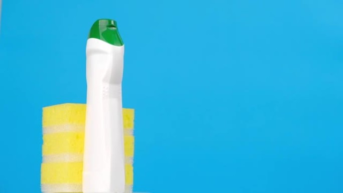 白色塑料瓶，带有洗涤剂和黄色海绵，用于洗碗，在蓝色背景上旋转。