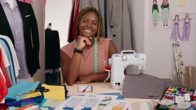 非裔美国女性裁缝微笑着自信地坐在裁缝店的桌子上