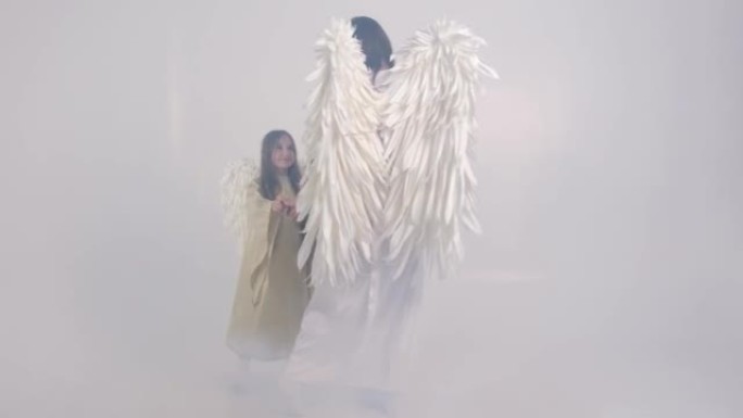 一个迷人的视频，一个母亲带着孩子在烟雾中以天使的形式带着白色的翅膀。4k视频