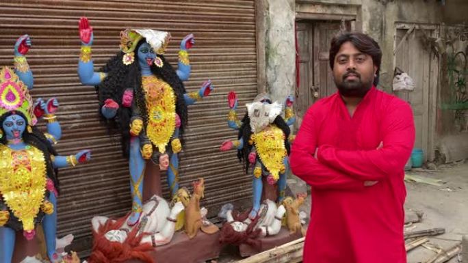 在加尔各答的路边车间里，一名穿着红色Kurta的印度男子站在卡利·马阿 (Kali Maa) 的偶像