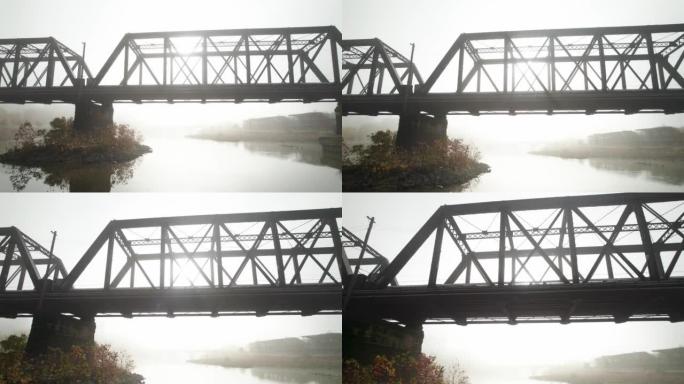 有雾和太阳耀斑的水上旧钢桥的鸟瞰图