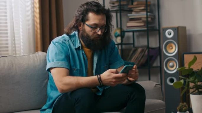 一个大胡子的帅哥和他的狗坐在客厅的沙发上。大胡子的人正在浏览智能手机上的保险单报价