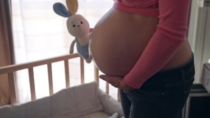 孕妇用针织兔子玩具关心她怀孕的肚子，快乐的妻子期待她的男婴在房间里准备基本必需品，女人怀孕的肚子，怀