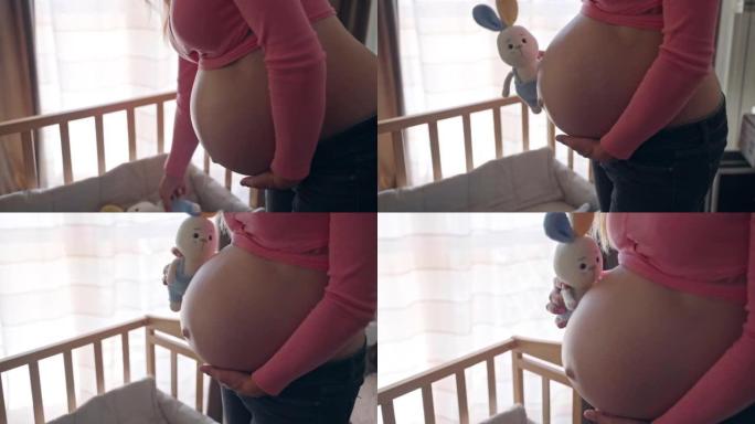 孕妇用针织兔子玩具关心她怀孕的肚子，快乐的妻子期待她的男婴在房间里准备基本必需品，女人怀孕的肚子，怀