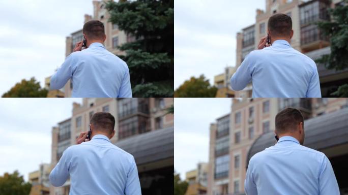 穿着衬衫的男人走在街上，用手机聊天。城市里的家伙的后方独自行走，用手机讲话。沟通。电话交谈。慢动作