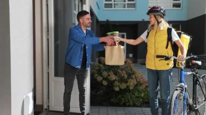 骑自行车的幸福女人用纸袋将咖啡和食物送到顾客家中。送餐概念。